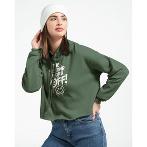 Könnte beinhalten: Ein dunkelolivgrüner, bauchfreier Kapuzenpullover mit weißem Grafikdruck, der THE SECOND WORD IS OFF! und ein tropfendes Smiley-Gesicht zeigt. Das Kleidungsstück hat eine Kapuze mit Kordelzug, lange Ärmel, eine blaue Jeans und eine weiße Mütze.