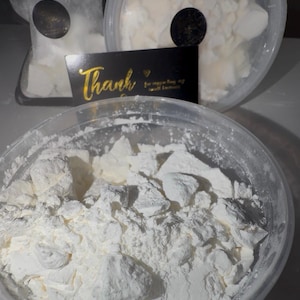 May include: A collection of white edible clay chunks and powder packaged in clear plastic containers. A black rectangular card with gold text reading Thank you for supporting my small business is placed in front of the containers.