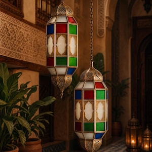 May include: Two hanging pendant lanterns featuring an intricate brass frame with geometric cutouts. Each lantern has panels of red, blue, green, and white glass arranged in a repeating pattern. The lanterns are suspended by metal chains.