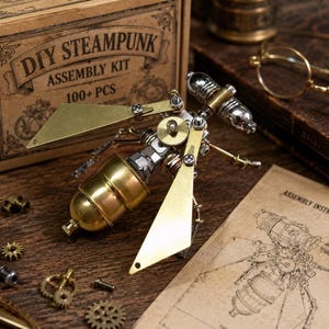 May include: A mechanical insect model constructed from metal components, including brass wings, a rounded brass abdomen, and silver-toned gear parts. The kit box is labeled DIY STEAMPUNK ASSEMBLY KIT 100+ PCS, accompanied by a printed assembly instruction sheet.