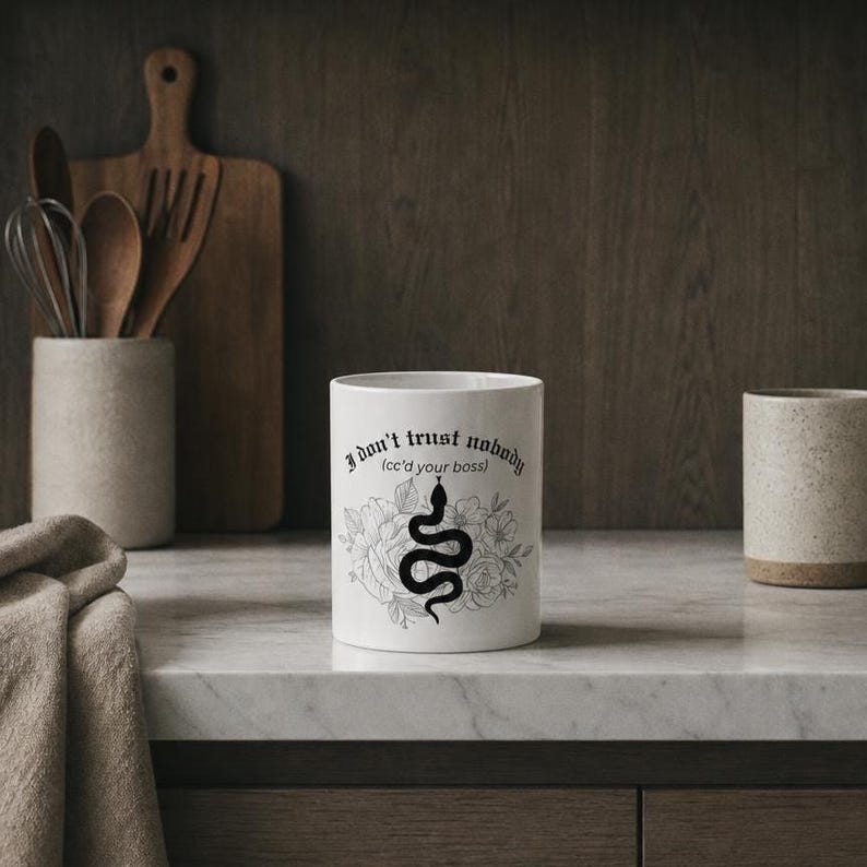 K&ouml;nnte beinhalten: Ein wei&szlig;er Keramikbecher mit einer schwarzen Grafik einer gewundenen Schlange, umgeben von floralen Linienzeichnungen. Der Text "I don't trust nobody (cc'd your boss)" ist in einer schwarzen gotischen Schrift &uuml;ber der Schlange aufgedruckt.