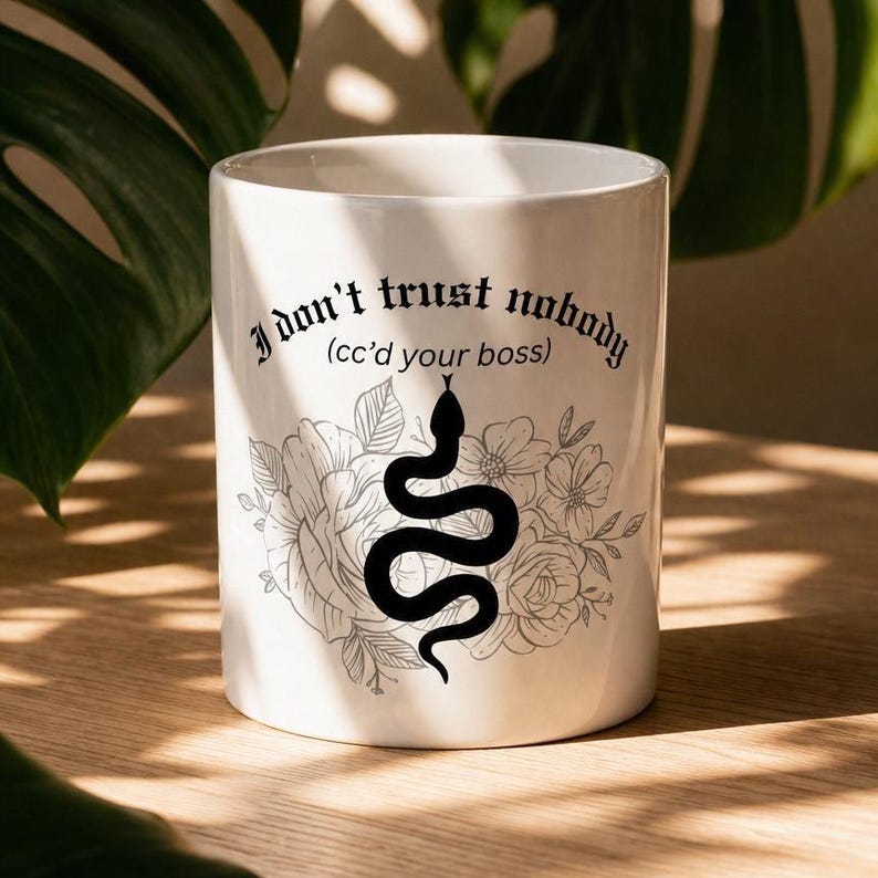 K&ouml;nnte beinhalten: Ein wei&szlig;er Keramikbecher mit einer schwarzen Grafik einer Schlange, die sich vor einer Blumenillustration windet. Der Text "I don't trust nobody (cc'd your boss)" ist in einer schwarzen gotischen Schrift &uuml;ber dem Schlangen- und Blumenmotiv gedruckt.