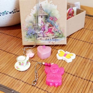 May include: A set of fairy-themed jewellery and accessories in a brown box. The set includes a pink heart charm, a pink fairy charm, a butterfly charm, a teacup charm, and a necklace with a clear glass bead.