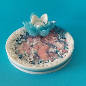 May include: A white ceramic dish with a blue and pink mosaic design. A blue and white ceramic lotus flower sits on top of the dish. The lotus flower has a small white candle holder in the centre.