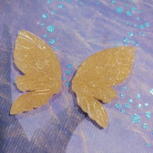 May include: A pair of gold glitter butterfly wings. The wings are translucent and have a delicate, intricate design.