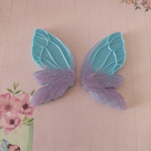 May include: Two blue and purple fairy wings with glitter. The wings are made of a lightweight material and have a delicate, whimsical design.