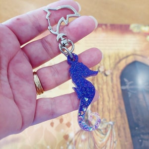 May include: A purple and iridescent glitter seahorse charm attached to a silver key chain.