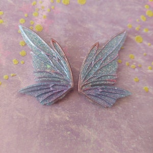 May include: Two iridescent blue and purple glitter fairy wings with a delicate, detailed design.