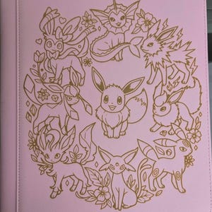 Puede incluir: Una carpeta de color rosa claro con una ilustración de líneas doradas de Eevee y sus diversas evoluciones dispuestas en forma de corona circular. El diseño incluye detalles florales y pequeñas formas geométricas alrededor.