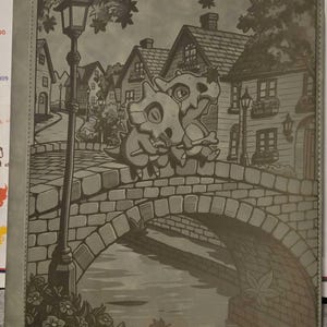 May include: A gray rectangular binder featuring a detailed monochromatic illustration of two Cubone characters sitting on a stone bridge. The scene includes a village with houses, a street lamp, and a stream below, all rendered in a consistent gray tone.