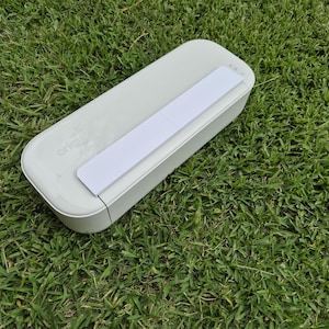 May include: A light gray, rectangular Cricut Joy electronic cutting machine with a smooth, rounded-edge plastic casing and a prominent white rectangular panel on the top surface, featuring the Cricut logo embossed on the left side of the device.