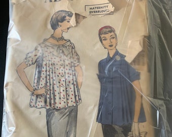 May include: Vintage sewing pattern for a maternity overblouse. The pattern shows two women wearing the overblouse, one in a polka dot print and the other in a solid blue. The pattern is labeled "Advance" and "Maternity Overblouse".