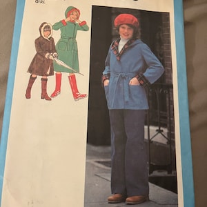 May include: Simplicity sewing pattern number 8838 for a girl's coat. The pattern includes two sizes, 12 and 14. The image shows a girl wearing a blue coat with a red and white checked lining and a red beret. The coat has a tie belt and pockets. The girl is wearing blue trousers and brown shoes.