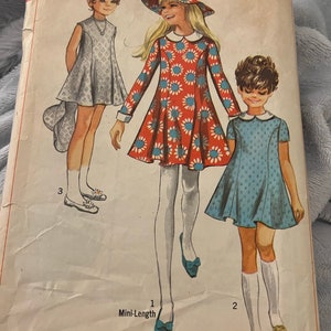 Puede incluir: Un patrón de costura vintage para un vestido corto para niña. El patrón muestra tres estilos diferentes de vestidos, uno con estampado floral, otro con estampado de lunares azul y blanco, y otro con un color azul sólido. El patrón está etiquetado como "Simplicing" y "7666".