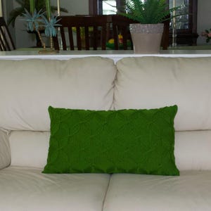 May include: A rectangular green decorative pillow with a textured leaf pattern rests on a cream-colored sofa. The pillow is the focal point, adding a pop of color to the neutral-toned furniture. The sofa is in a well-lit room.
