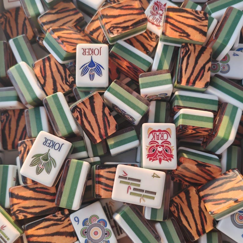 May include: A collection of rectangular mahjong tiles featuring a mix of tiger-striped backs and white faces. Some tiles display the word JOKER with a blue flower icon, others show a red dragon face with the text CRAK, or green bamboo symbols.