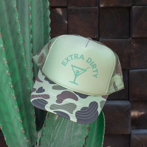 May include: A green and camouflage trucker hat with the text "EXTRA DIRTY" and a martini glass graphic.