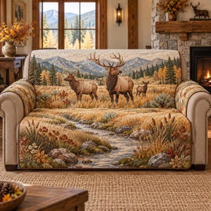 May include: A quilted sofa cover featuring a scenic landscape print of a flowing stream, rocky banks, and tall grasses in the foreground. The backrest displays a mountain range with pine trees and three elk standing in a golden meadow.