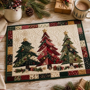 May include: A rectangular quilted placemat featuring three appliqued Christmas trees in shades of red, green, and gold. The center is cream-colored with swirling stitch patterns, surrounded by a border of small, multi-colored fabric squares.