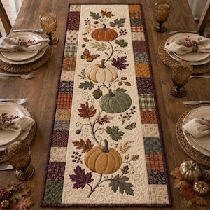 May include: A rectangular quilted table runner featuring a central cream panel with embroidered pumpkins in orange, white, and green, surrounded by autumn leaves, acorns, and a butterfly. The border consists of a patchwork of small fabric squares.