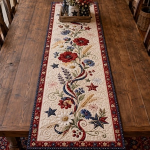 May include: A long, rectangular quilted table runner featuring a cream-colored center with a floral and star pattern in red, white, and blue. The design includes poppies, daisies, wheat stalks, and stars, bordered by a red and blue patterned trim.