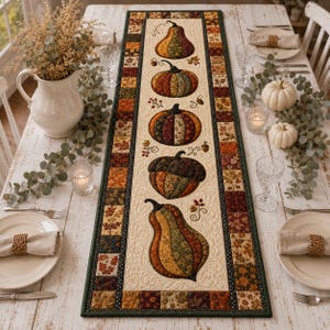 May include: A rectangular quilted table runner featuring a central cream panel decorated with five appliqued pumpkins and gourds in various autumn colors and patterns, surrounded by a border of small squares with fall leaf motifs.