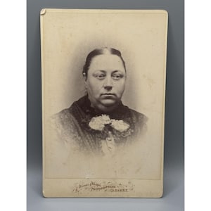 May include: A sepia-toned cabinet card photograph featuring a portrait of a person with hair parted in the center, wearing a dark textured garment with a light-colored lace collar. The bottom edge includes the text Winsor & Whipple Photographers Olean N.Y.