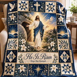 May include: A rectangular quilt featuring a central image of a figure in white and blue robes standing before a stone tomb with a sunrise background. The border includes white lilies, doves, stars, and a cross. Text reads: He Is Risen Hope Has Dawned.
