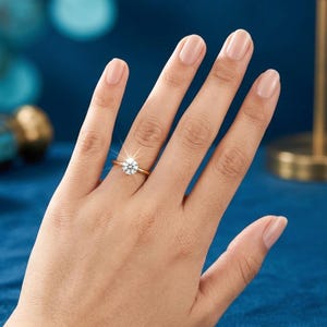 Puede incluir: Un anillo de oro con una piedra preciosa transparente de talla brillante redonda, montada en un engaste clásico de cuatro garras. La banda es fina y pulida, mostrando una superficie brillante y reflectante que capta la luz.