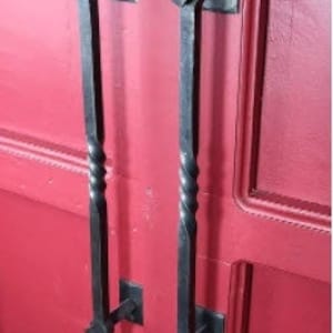 以下が含まれることがあります： ねじれたデザインの黒い金属製のドアノブのペア。ノブは赤いドアに取り付けられています。