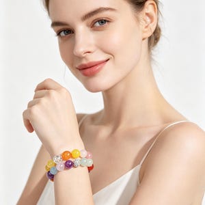 May include: A multi-coloured beaded bracelet featuring round polished stones in shades of yellow, orange, pink, purple, blue, and green, accented with two spherical charms encrusted with small clear crystals, worn on a wrist.