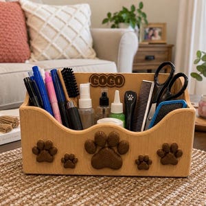 K&ouml;nnte beinhalten: Ein hellbrauner Schreibtisch-Organizer aus Holz mit strukturierter Oberfl&auml;che und f&uuml;nf braunen Pfotenabdruck-Motiven auf der Vorderseite. Auf der R&uuml;ckwand ist der Name COCO in erhabenen braunen Buchstaben angebracht. Er enth&auml;lt Stifte und Utensilien.