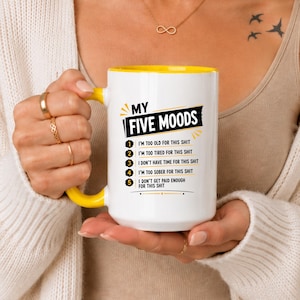 May include: A white ceramic mug with a bright yellow handle and interior rim. The front features black text that reads MY FIVE MOODS followed by a numbered list of five statements ending in the word shit, accented with yellow graphic lines.