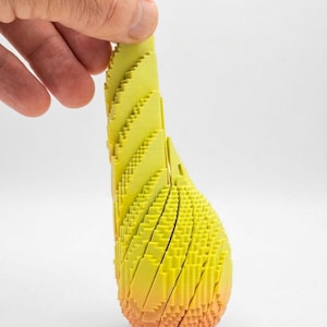 May include: A 3D printed object with a vertical, elongated, teardrop-like shape. The structure features a layered, stepped texture with a gradient color transition from a bright yellow at the top to a warm orange hue at the base.