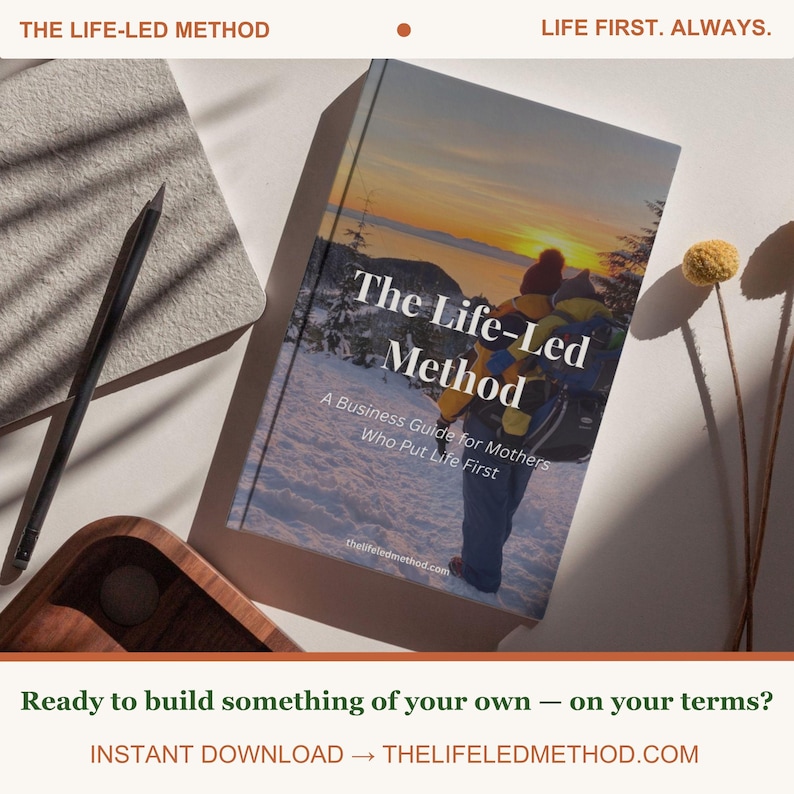May include: A book titled The Life-Led Method: A Business Guide for Mothers Who Put Life First, featuring a cover image of a person carrying a child on their back in a snowy landscape at sunset, with the website thelifeledmethod.com printed below.