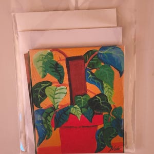 May include: An original painting of a potted plant with green and blue leaves, a red pot, and a brown support structure. The background is orange. The artwork is signed "Wala" in the lower right corner. The painting is packaged in a clear plastic sleeve with white backing.