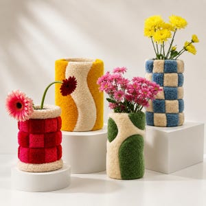 Puede incluir: Cuatro jarrones cilíndricos con textura de mechones y patrones distintos. Uno presenta un diseño de cuadros rojos, otro un patrón ondulado amarillo y crema, un tercero una forma orgánica verde y crema, y el último un patrón de cuadros azules y crema.