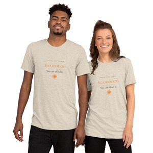 Può includere: Una t-shirt a maniche corte color beige mélange con il testo "THANK YOU" COSTS $0.000006 You can afford it. stampato in arancione, accompagnato da una piccola icona di sole arancione centrata sotto il testo sul davanti.