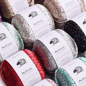 May include: Multiple skeins of metallic yarn in various colors including red, black, silver, and teal, each wrapped in a white paper band labeled MuYuan Frost Words with a black sheep icon, featuring a shimmering texture with small sequins.