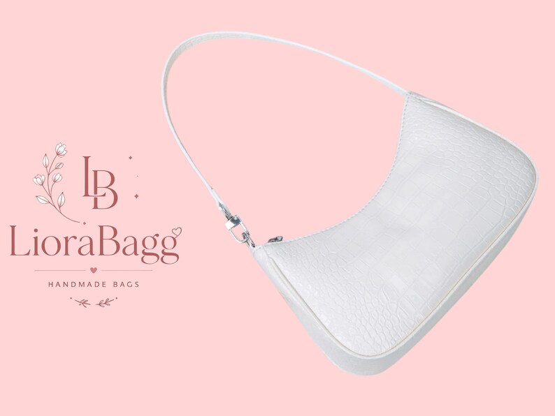 May include: A white shoulder bag with a textured crocodile skin pattern, a single strap, and a silver-toned zipper closure. The text LioraBagg HANDMADE BAGS with a floral logo is visible to the left of the bag on a light pink background.