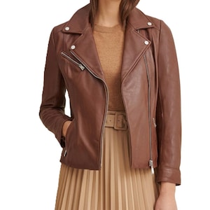 May include: A brown leather biker jacket featuring a notched collar, silver-toned metal zips on the front and pockets, and snap button details on the lapels. The jacket is worn over a tan jumper and a pleated skirt with a matching belt.