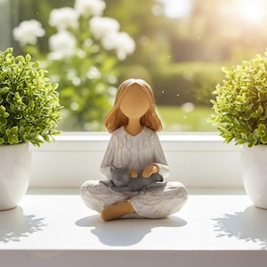 May include: A figurine of a person with long brown hair sitting in a cross-legged position, wearing a white long-sleeved garment with a textured crackled finish, holding a small gray cat in their lap with both hands.