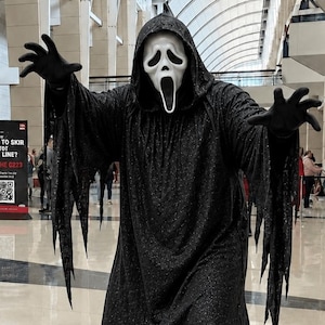May include: A full-length black hooded robe with jagged, tattered edges on the sleeves and hem, paired with a white Ghostface mask featuring a long, open-mouthed expression and black eye sockets, worn with black gloves and black shoes.