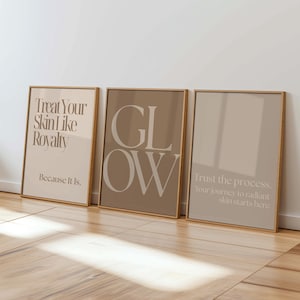 Peut inclure: Trois affiches encadrées avec des fonds beige et brun clair. La première affiche porte l'inscription "Treat Your Skin Like Royalty Because It Is". La deuxième affiche présente le mot "GLOW" en grandes lettres. La troisième affiche indique "Trust the process. Your journey to radiant skin starts here."