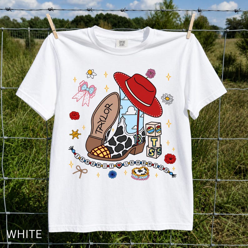 May include: A white short-sleeve t-shirt featuring a graphic print of a cow-print cowboy boot, a red cowboy hat, blocks with the letters T, S, and a heart, and a beaded string with the text I KNEW IT I KNEW YOU and the name TAYLOR.