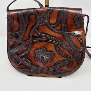 Può includere: Una borsa a tracolla in pelle marrone con un design in rilievo di cavalli e intricati motivi a cinghia. La borsa presenta una patta arrotondata, una lunga tracolla e una finitura scura e lucida con incisioni dettagliate sul davanti.
