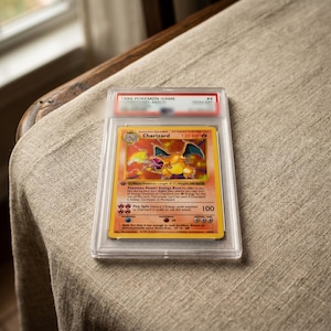 May include: A 1999 Pokemon Game Charizard trading card encased in a clear protective plastic slab. The card features the orange dragon-like creature with blue wings, 120 HP, and the Fire Spin attack. The label at the top reads 1999 POKEMON GAME #4.