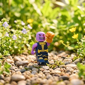 Könnte beinhalten: Eine violette Thanos-Minifigur mit einem dunkelblauen und goldenen Torso- und Beindesign. Die Figur hat einen lächelnden Ausdruck mit roten Augen und einen erhobenen goldfarbenen Handschuh an der linken Hand. Die Figur steht aufrecht im kleinen Maßstab.