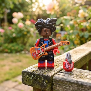 Op de afbeelding: Een plastic minifiguur met donker haar, gekleed in een zwart vest over een blauw shirt en een rode broek, met een oranje elektrische gitaar met stickers. Naast het figuur staat een los rood hoofd met een zilveren hanenkam en webpatroon.