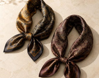 May include: Two square neck scarves featuring intricate paisley patterns. One scarf displays a gradient of gold and black, while the other is a deep chocolate brown. Both scarves are tied in a knot, showcasing a smooth, satin-like finish.